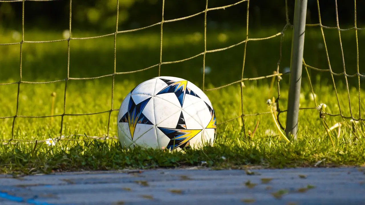 Bola de futebol sobre a grama, junto à rede de um gol.