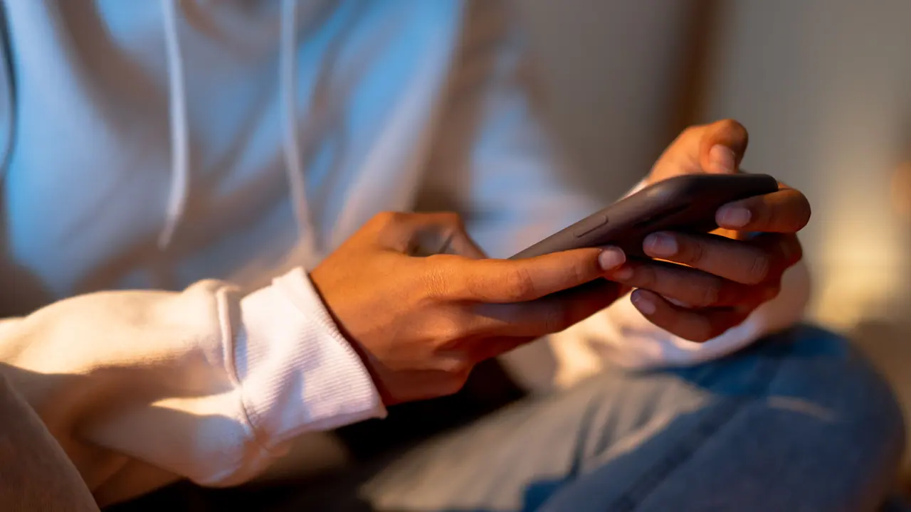 Mãos de uma pessoa usando um smartphone em ambiente interno.
